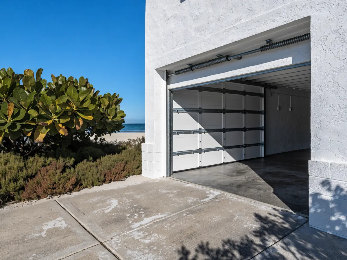Impact-rated steel garage door on a concrete block house near the coast, heavy reinforcing struts visible through the open door