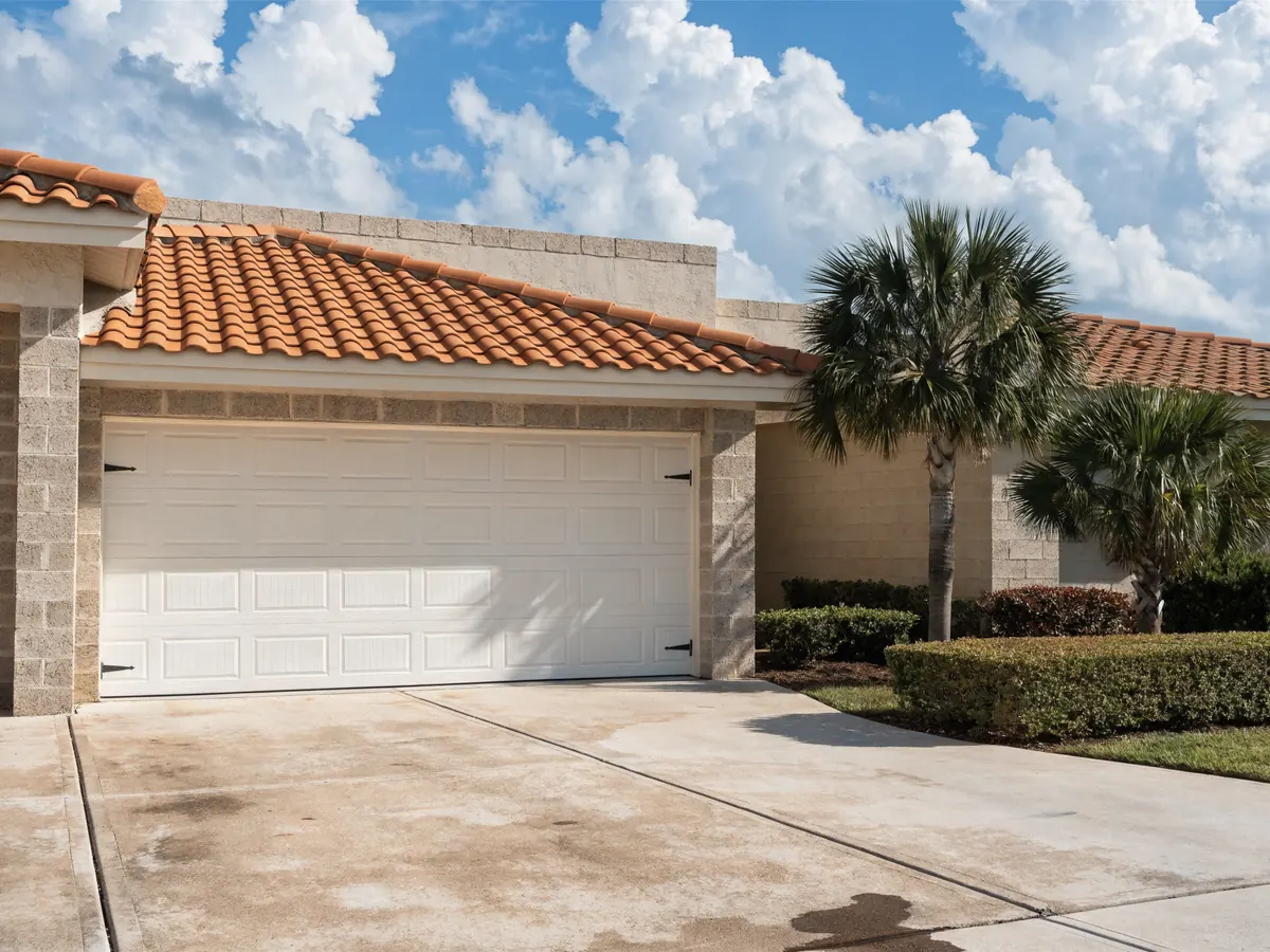 Wind rated white steel garage door with short raised panels, closed on a single storey concrete block and stucco house with a barrel tile roof and sabal palms