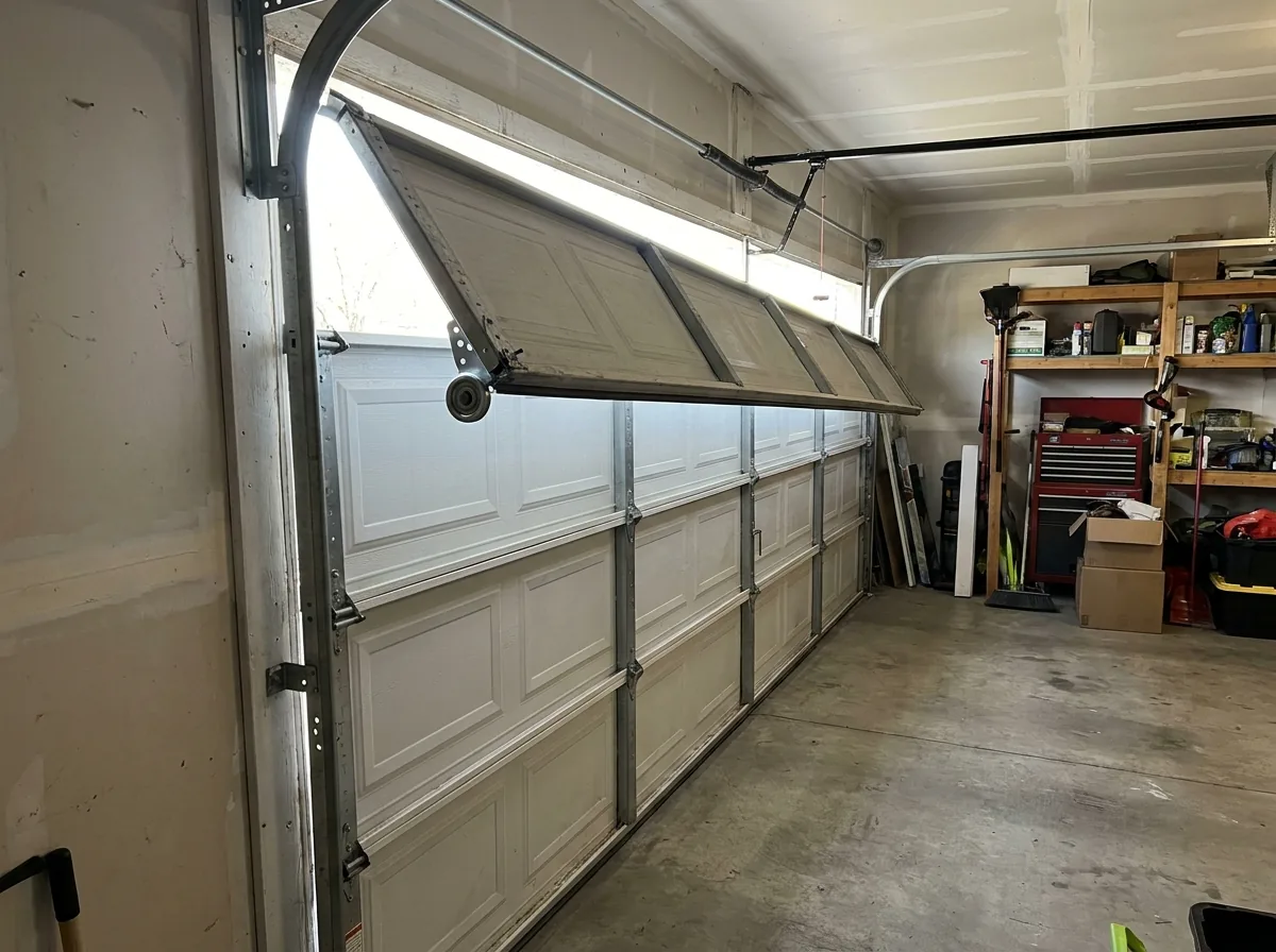 Garage door with the top section pulled out of its vertical track and leaning inward, the roller clearly out of the rail