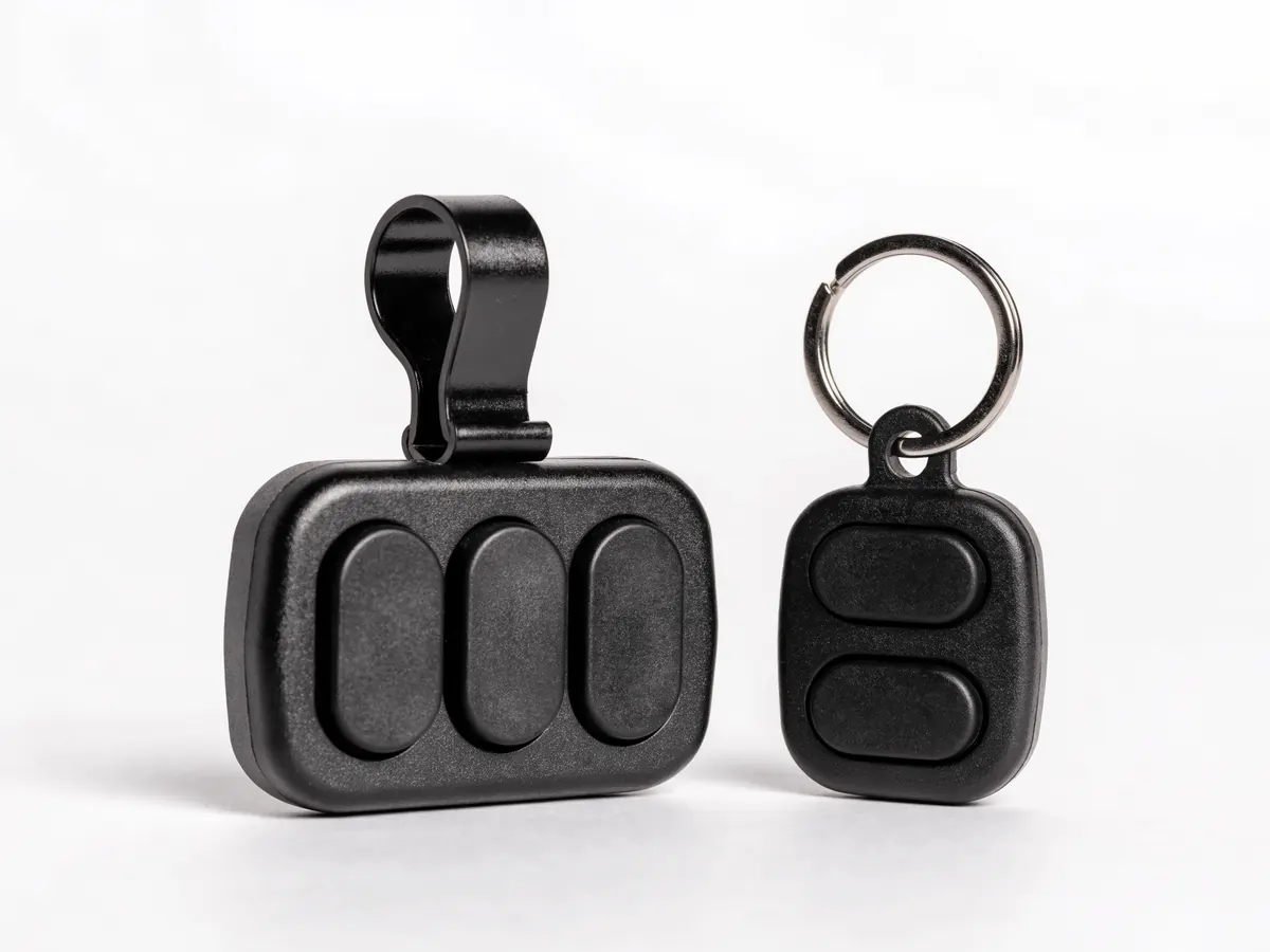Two garage door remotes, a three button visor remote with a metal clip and a smaller two button keyfob on a split ring